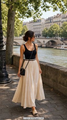 Woman in a long skirt and tank top walking along a river in a city