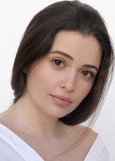 Woman with long dark hair wearing a white shirt, looking directly at the camera
