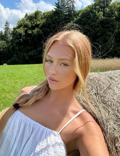 Woman with blonde braided hair in a white top next to a hay bale in a field