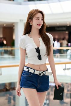 Woman in a white crop top and denim shorts with a cow print belt indoors