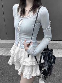 Person in a light blue long sleeve top and white ruffle skirt with a black shoulder bag