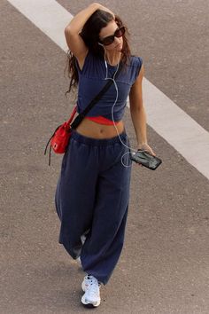 Woman in a crop top and sweatpants walking on a street with earbuds