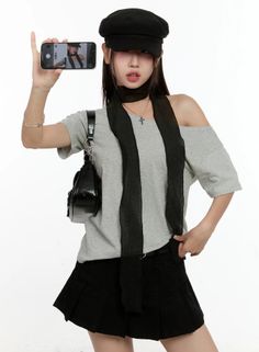 Woman in a black cap and off-shoulder top holding a phone to take a picture