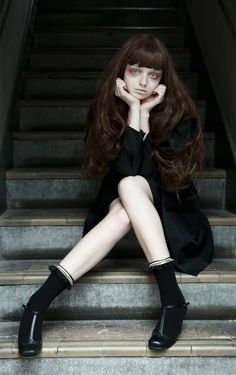 Woman with long hair and pale skin sitting on stairs in a dark dress