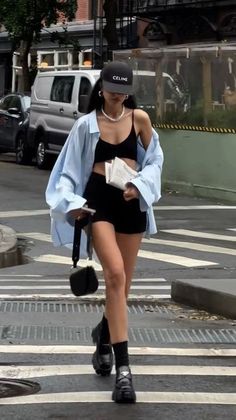 Woman in a black bra top and shorts with an oversized blue shirt walking on a street