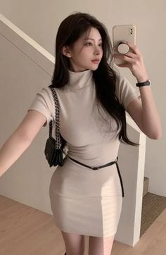 Woman in a beige turtleneck mini dress taking a selfie indoors