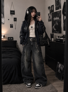 Woman in a hoodie and baggy jeans taking a mirror selfie indoors