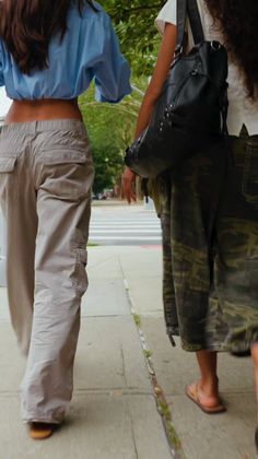 Two people walking on a sidewalk, one in a crop top and cargo pants
