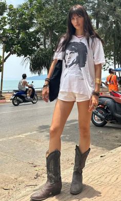 Woman in a white t-shirt and cowboy boots standing on a street