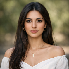 Woman with long dark hair wearing an off-shoulder top and gold jewelry outdoors