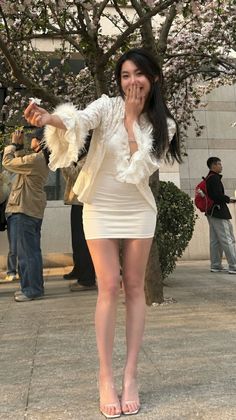 Woman in a white dress and high heels posing outdoors with cherry blossoms