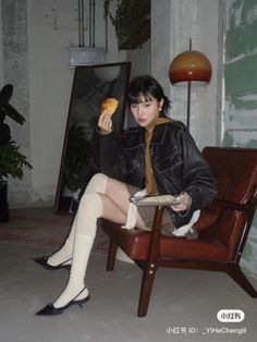 Woman in a leather jacket and thigh-high socks sitting in a brown chair indoors