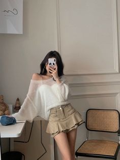 Woman in a white sweater and mini skirt taking a mirror selfie indoors