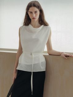 Woman with long hair wearing a white belted top and black skirt indoors