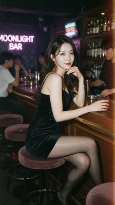 Woman in a black dress sitting at a bar with neon lighting