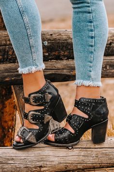 Person wearing black buckle heels and light wash jeans on a wooden log