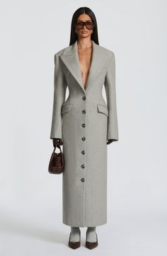 Woman in a long grey coat and sunglasses holding a small brown bag