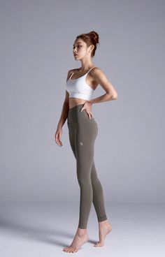 Woman in a white sports bra and olive yoga pants posing in a studio
