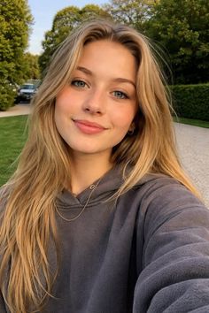 Young woman with long blonde hair and blue eyes wearing a hoodie outdoors