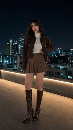 Woman in a brown jacket and pleated skirt with knee high boots on a rooftop at night