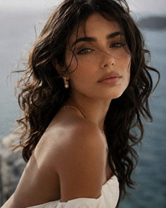 Woman with long wavy hair and pearl earrings in an off-shoulder top outdoors