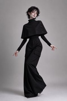 Person with short black hair in a black turtleneck, cape, and wide-leg pants