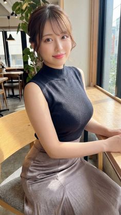 Woman in a black sleeveless top and long skirt sitting at a table indoors