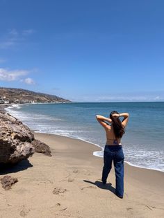 Woman with long hair standing on a sandy beach looking out at the ocean