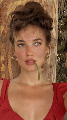Woman with freckles and a messy bun, wearing a red top and gold jewelry