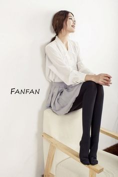 Woman in a white blouse and pleated skirt sitting on a chair indoors