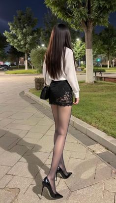 Woman with long dark hair in a black mini skirt and high heels at night