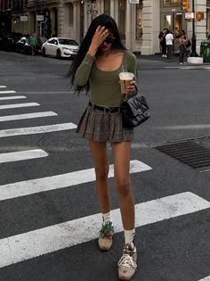 Woman in a plaid skirt and long-sleeve top crossing a city street