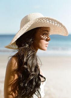 Woman in a straw hat with sunlight creating patterns on her face at the beach