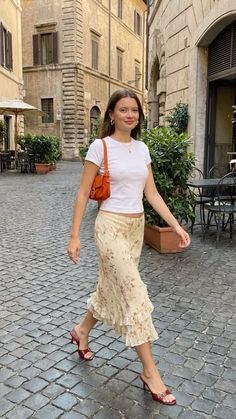 Woman in a white t-shirt and floral skirt walking on a cobblestone street