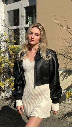 Woman with blonde hair wearing a black leather jacket and ribbed dress outdoors
