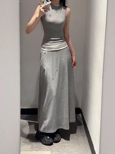 Person in a gray sleeveless top and long skirt taking a mirror selfie