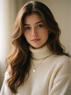 Woman with long brown hair wearing a cream turtleneck sweater and gold necklace