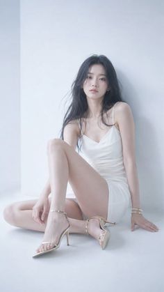 Woman in a white slip dress and gold high heels sitting on a light floor