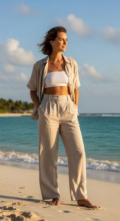 Woman in a white bandeau top and linen pants on a beach at golden hour
