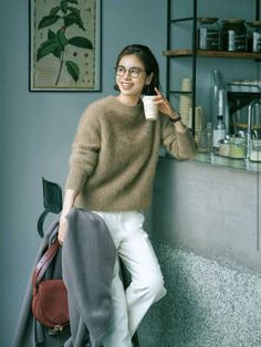 Woman in a brown sweater and white pants smiling in a cafe