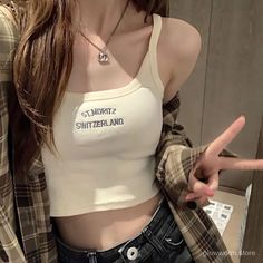 Person in a plaid shirt and crop top making a peace sign indoors
