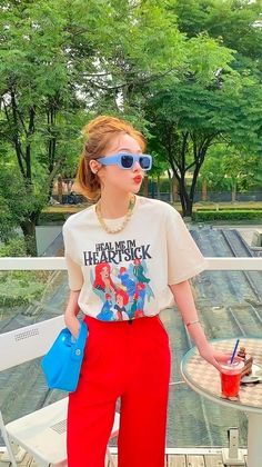Woman in red pants and a graphic t-shirt wearing blue sunglasses outdoors