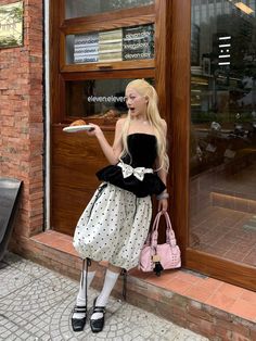 Woman with blonde hair in a polka dot skirt and strapless top holding a croissant
