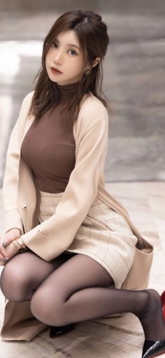 Woman in a brown turtleneck and plaid skirt kneeling indoors