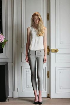 Woman with long blonde hair wearing a white top and grey pants indoors