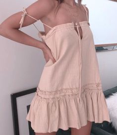 Woman in a light pink mini dress with ruffle trim and layered necklaces