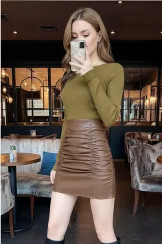Woman in a brown skirt and olive top taking a mirror selfie indoors