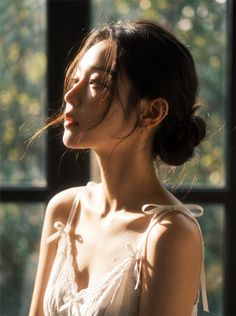 Woman in a white top with a messy bun, bathed in soft sunlight indoors