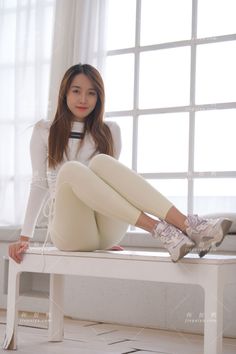 Woman with long hair wearing a white top and leggings, sitting indoors