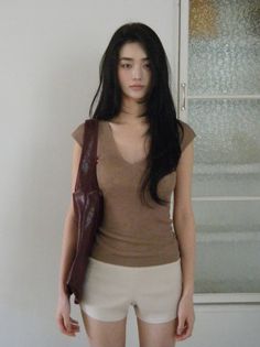 Woman with long black hair wearing a brown top and white shorts indoors